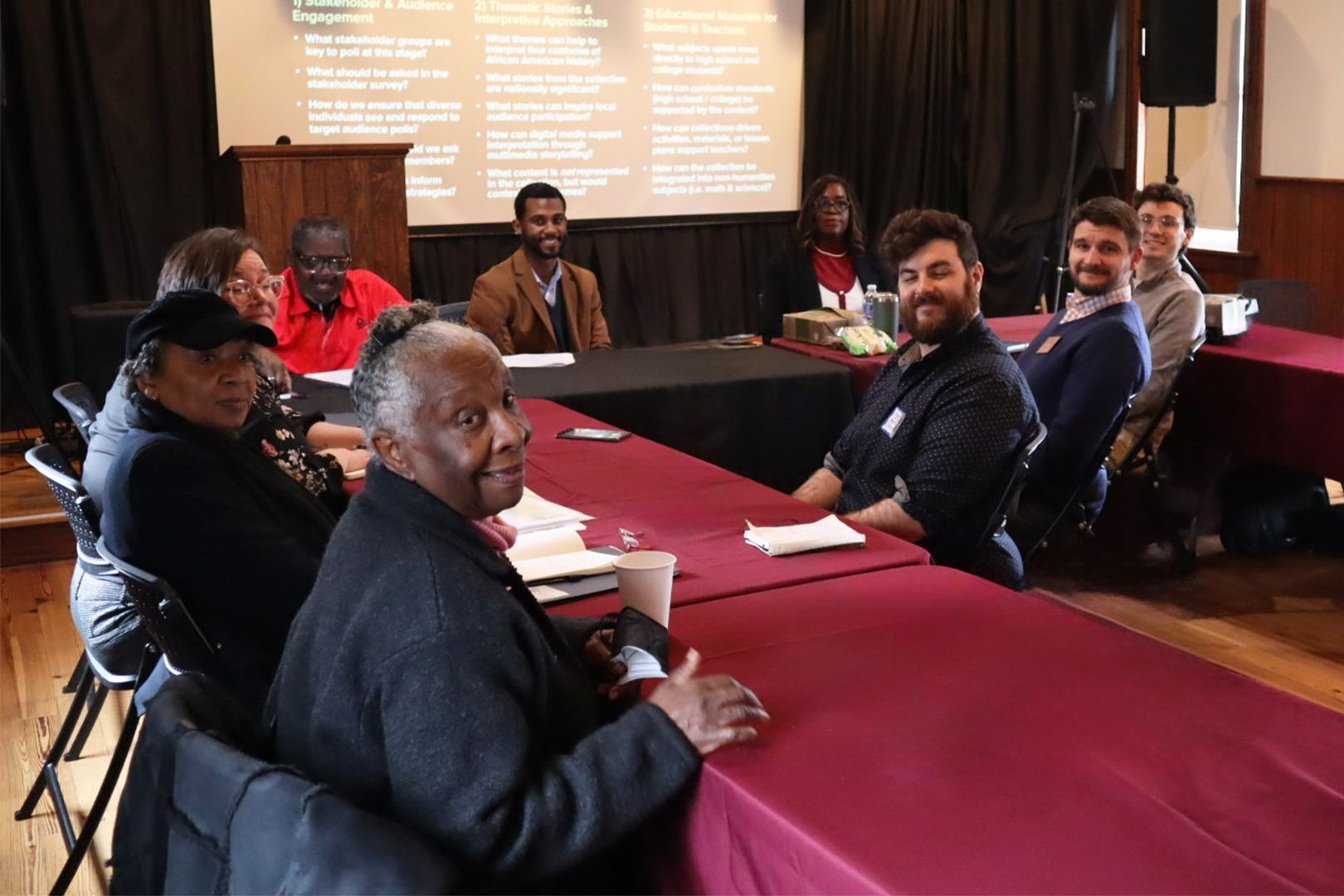 A group of people sitting around tables in a conference room, turned to look at the camera and smiling